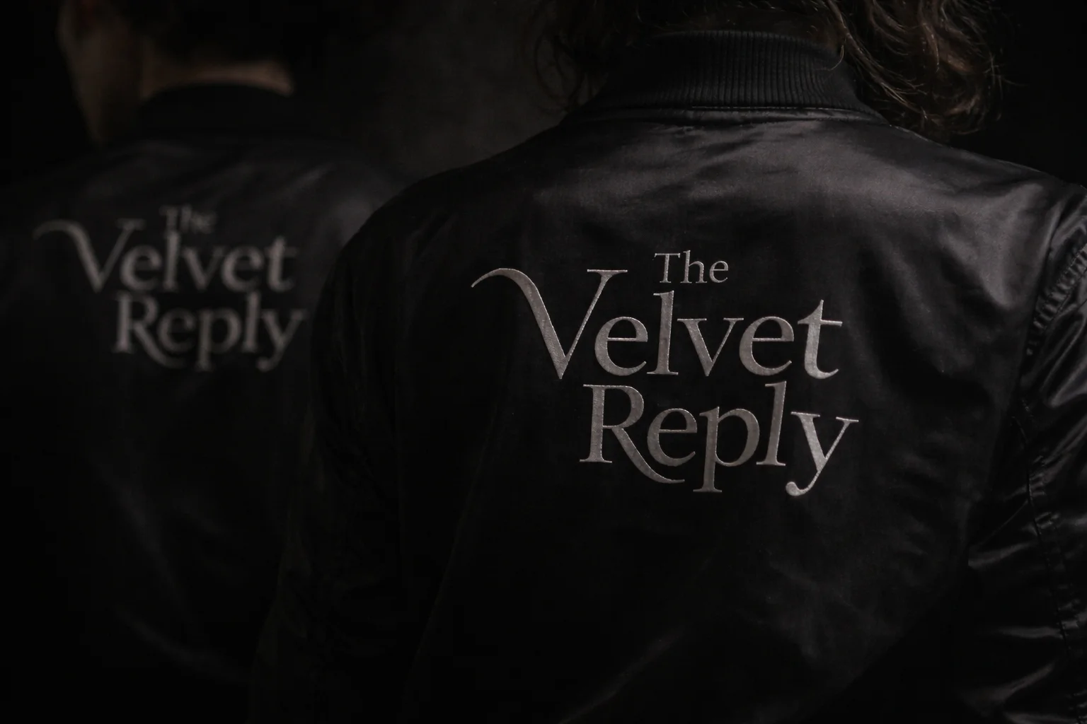Black satin bomber jacket with silver The Velvet Reply embroidery on the back